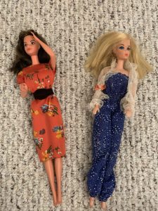 Two Barbie dolls, a brunette in a very late-70s floral dress and a blonde in a strapless blue jumpsuit.