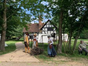 A half-timbered English farm building from the 16th century, with reenactors wearing costumes from the early 1600s standing in front.