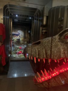 An old-fashioned bank vault full of treasure is guarded by a dragon so large that only its mouth with glowing red teeth shows.