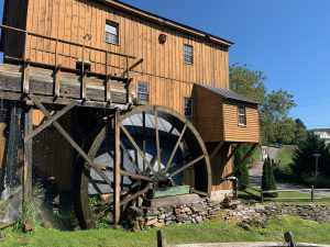 A big mill made of golden-toned wood, with a water wheel on the side. The sky is a bright blue.