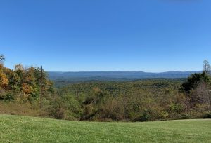 A view from a mountain pass, with lower mountains and the start of fall color in front and the blue ridge of the Blue Ridge Mountains in back, with a bright blue sky overhead.