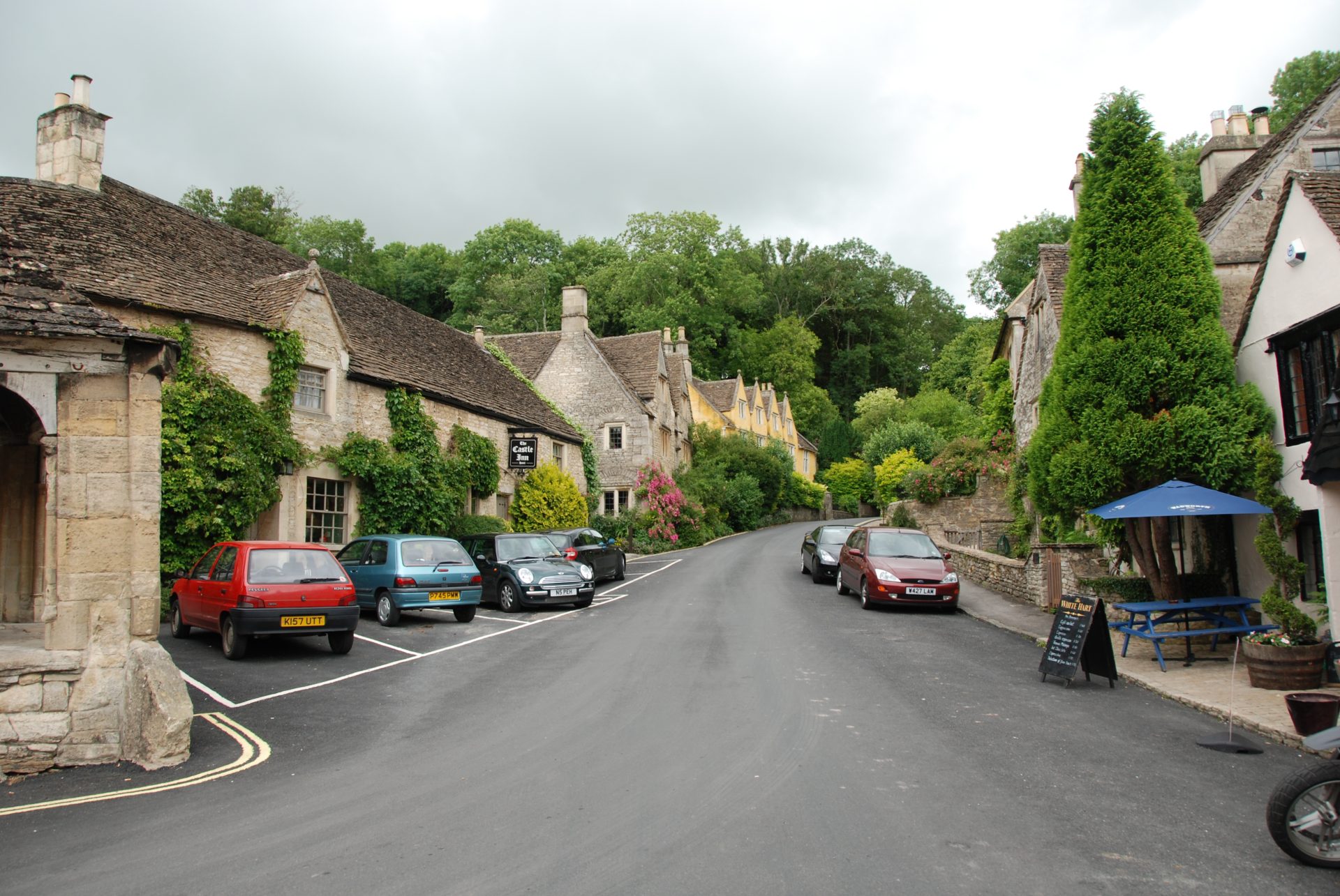 A village lane leading away from the market square, old buildings nestled together. There are trees in the distance.