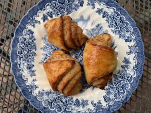Three rolls with layers of cinnamon showing sit on a blue-and-white plate