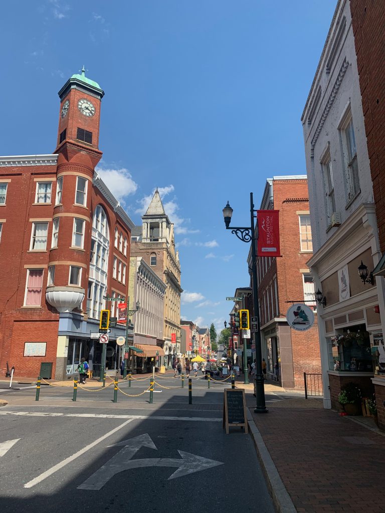 A quaint Victorian small-town Main Street. To the right, there's a small storefront with display windows and a sign hangs overhead showing a dragon curled up on a stack of books.