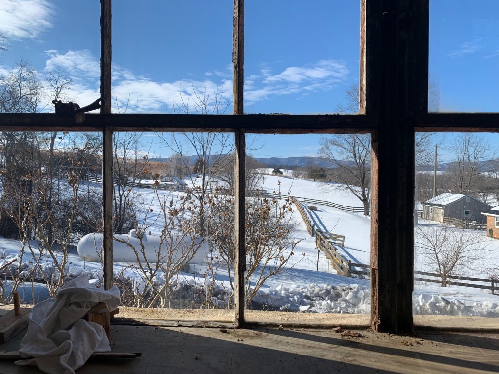 The view through an old square-paned window, with rolling hills covered in snow in the foreground and mountains in the distance.