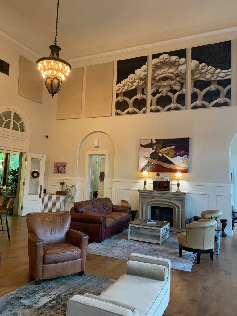 The interior of a Beaux Arts train station, with ornate chandeliers and comfy chairs by a fireplace.