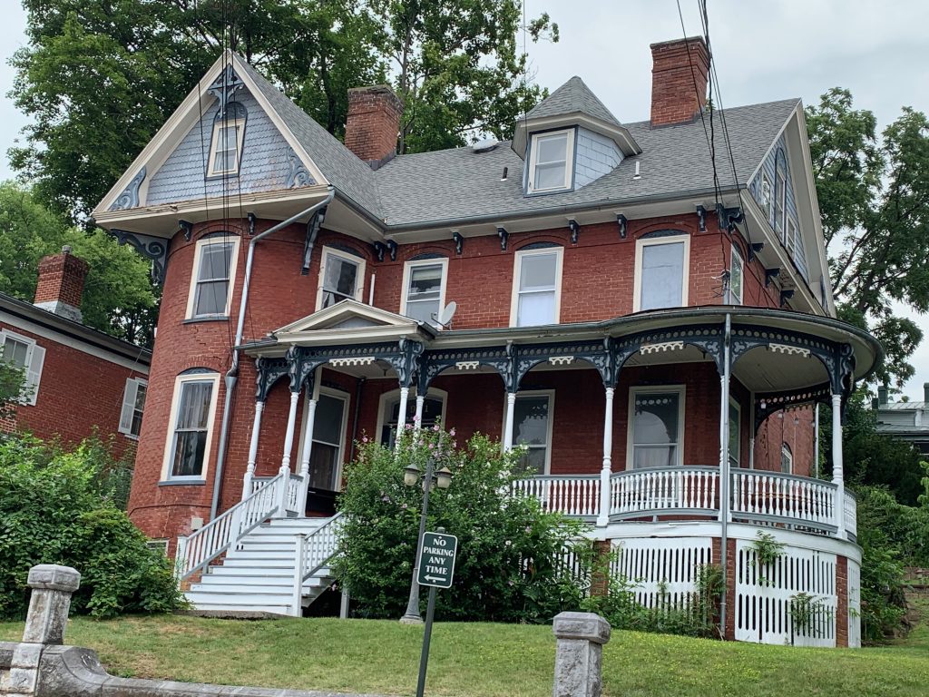 A red brick Victorian house with a turret on one side and a wrap-around porch.